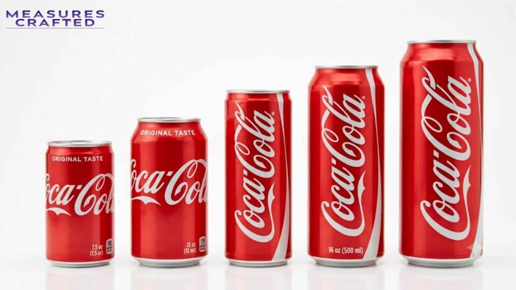Five red Coca-Cola cans lined up on a white surface. Ranging in height from smallest to tallest, left to right.