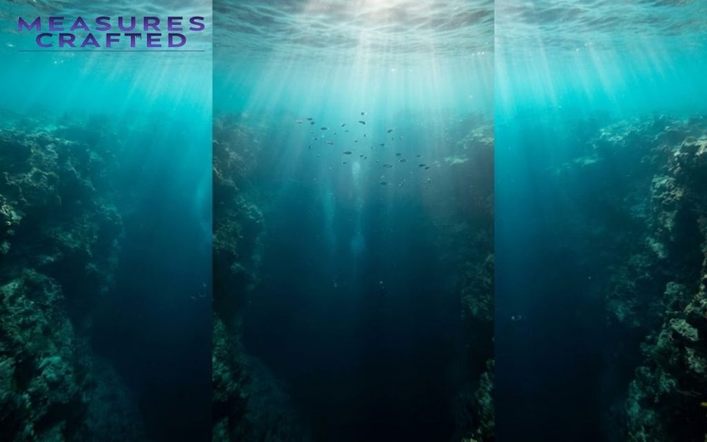 Sunlight rays filter through a underwater chasm. A small school of fish swims between dark, craggy canyon walls.