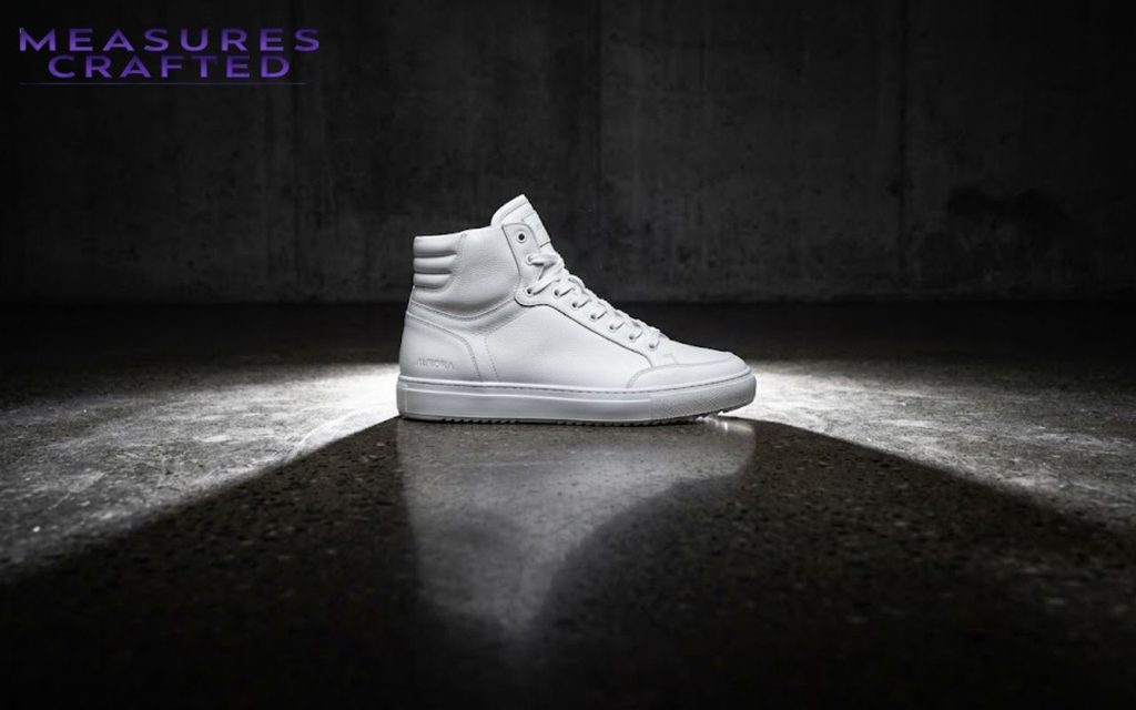 A single white Aurora high-top sneaker. Profile view, dramatically spotlighted on dark concrete.
