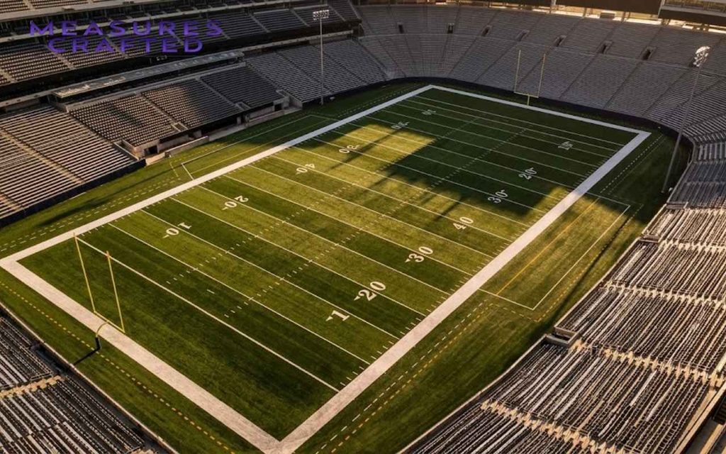 Aerial view of an empty football field with crisp yard lines showing a scale of about 100 feet.