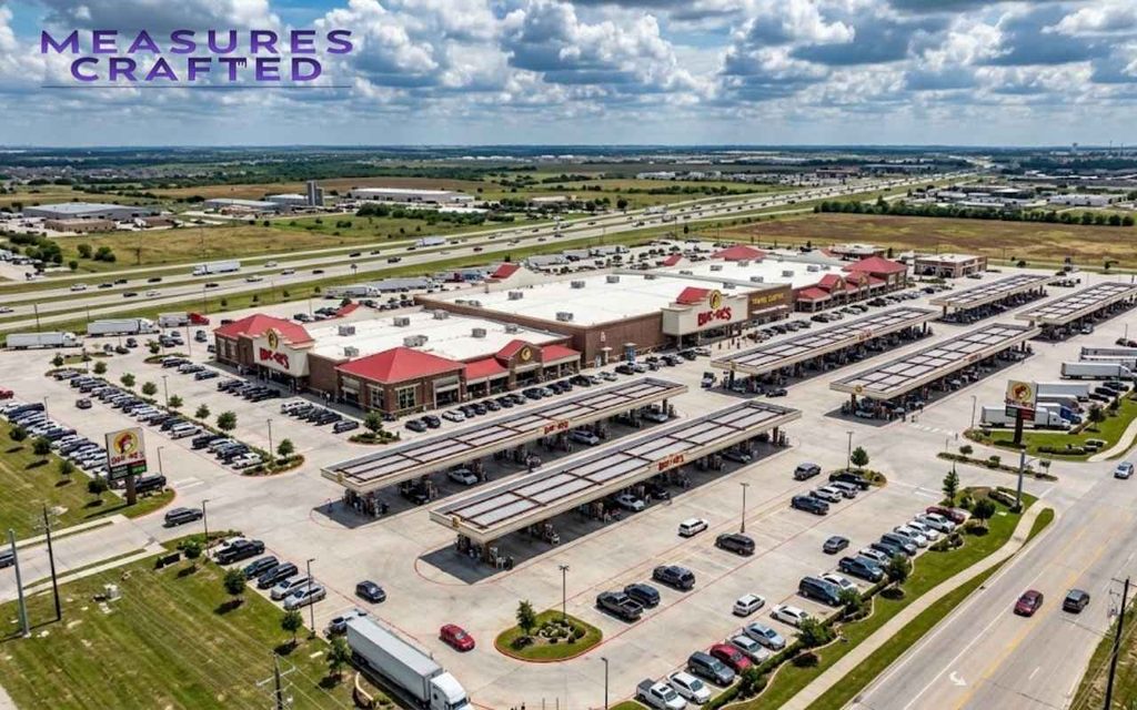 Aerial view of a massive roadside travel center, gas pumps, and parking lot under a cloudy sky.
