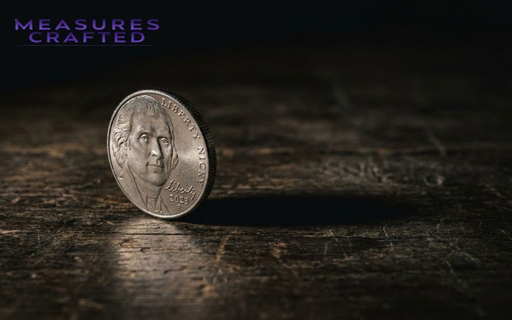 A US Jefferson 2mm-thick nickel stands upright on a dark wood surface, showing the 2023 date.
