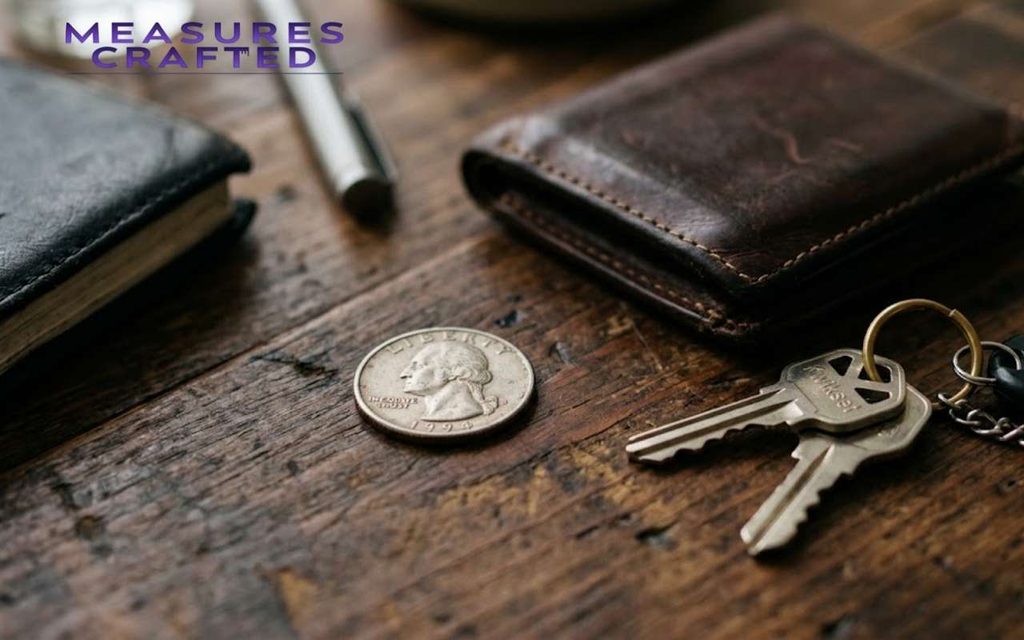 Close-up of a wooden desk with a leather wallet, a 1994 quarter, keys, a pen, and a black notebook.