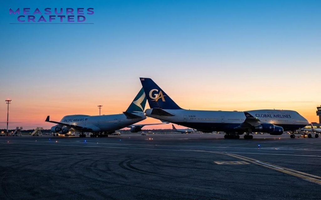 Two large commercial airplanes with prominent blue tail fins are parked nose-to-tail on an airport tarmac at sunset.