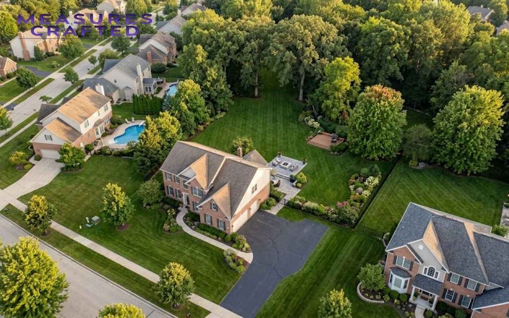 An aerial view of a large house and a yard with trees that extend back over 100 feet.