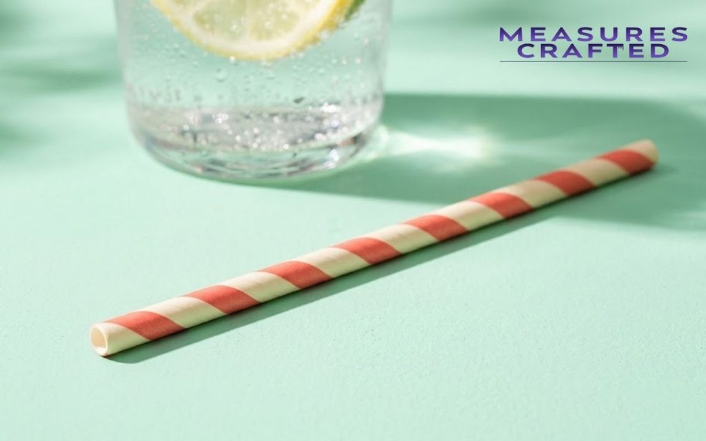 A cream-and-coral striped paper straw diagonally on a mint-green surface with citrus water.